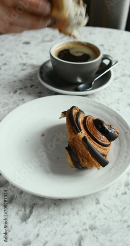 Close-up of dunking a half of freshly baked chocolate croissant into a cup of hot black coffee