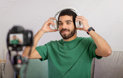 Content creator in a casual green t-shirt enjoys music on white headphones, smiling at the camera