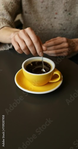 Unrecognizable caucasian woman in a cozy sweater drinking a cup of hot black coffee, sitting at the table