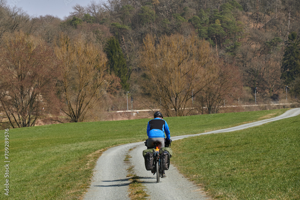 Obraz premium Radfahrer in langer Radbekleidung auf einem Tourenrad mit Packtaschen auf einem geschotterten Abschnitt des Lahn-Radweges