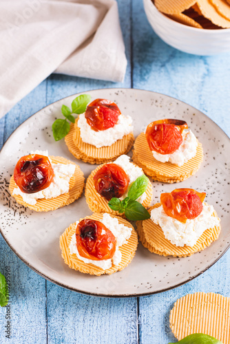 Crostini on crispbread with ricotta, baked tomatoes and basil on a plate vertical view