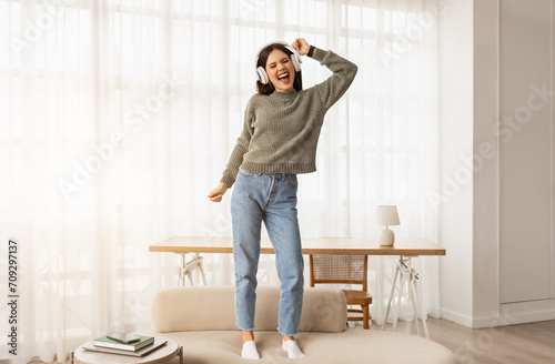 Carefree young woman dancing on couch, listening to music