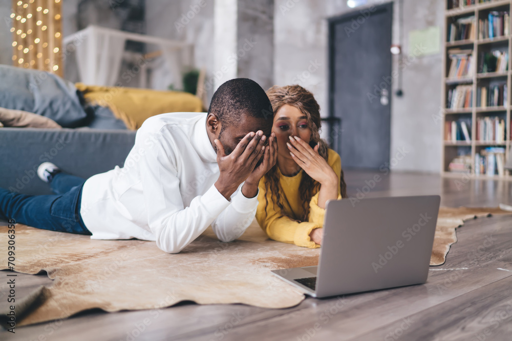 Couple in shock and excitement while looking at their laptop  computer screen, dramatic reaction on bank email in comfort of trendy living space, with soft festive lighting adding to the ambiance