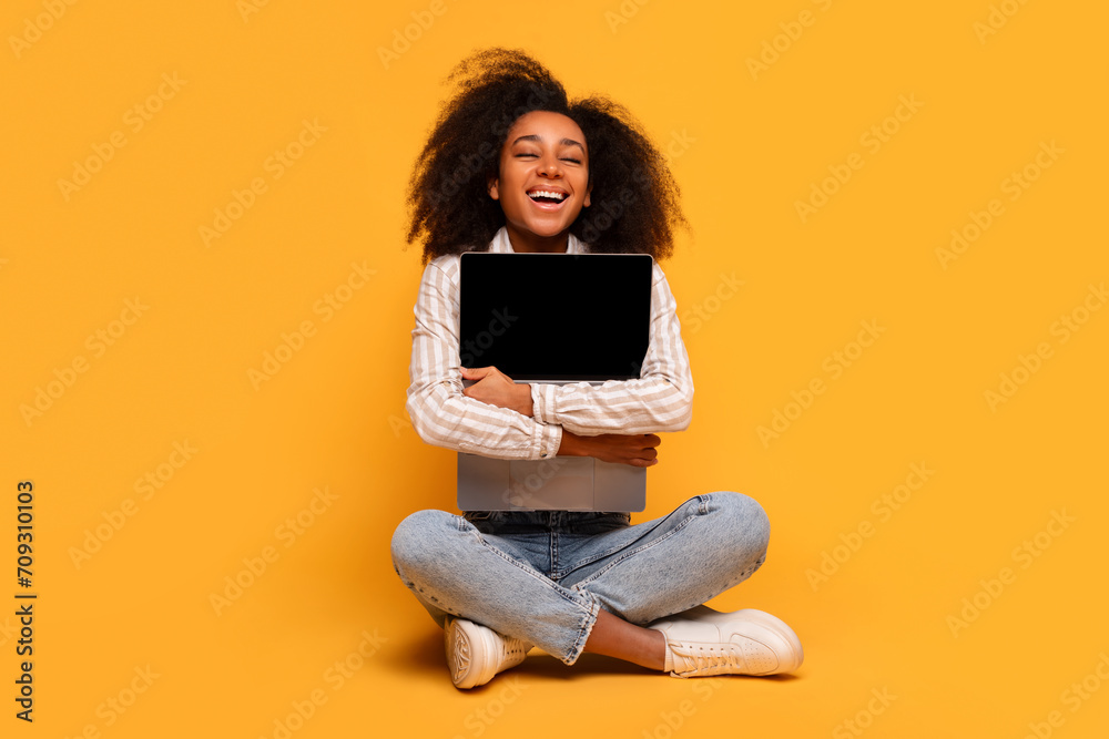 Happy young black woman holding laptop on yellow background Happy young black woman holding laptop on yellow background