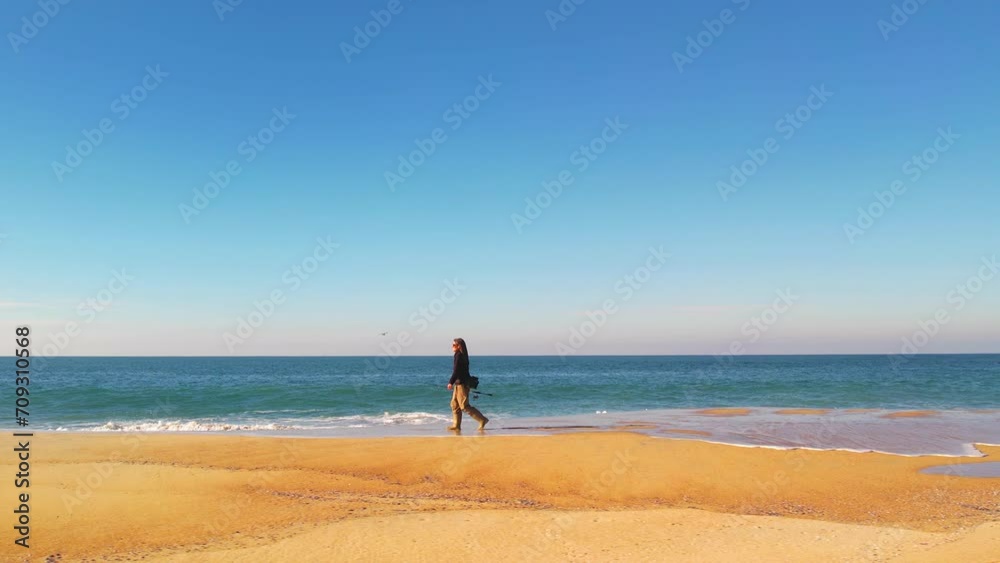Fisherwoman walking on a beach, near the sea, with her fishing tackle Fisherwoman walking on a beach, near the sea, with her fishing tackle
