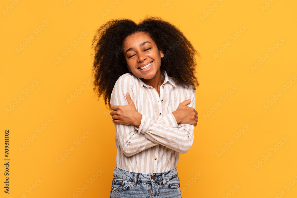 Content woman hugging herself with joyful smile, yellow background Content woman hugging herself with joyful smile, yellow background