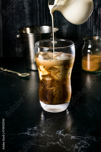 An enticing glass of Greek frappe mid-preparation, with a stream of milk being poured, creating a beautiful swirl in the combination of instant coffee and ice photo