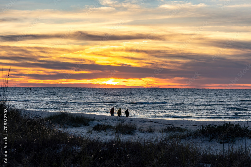 Silhouette of three people walking along the ocean on a beach at sunrise. Silhouette of three people walking along the ocean on a beach at sunrise.