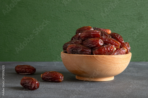 Date fruits in wooden bowl,on green background
 photo