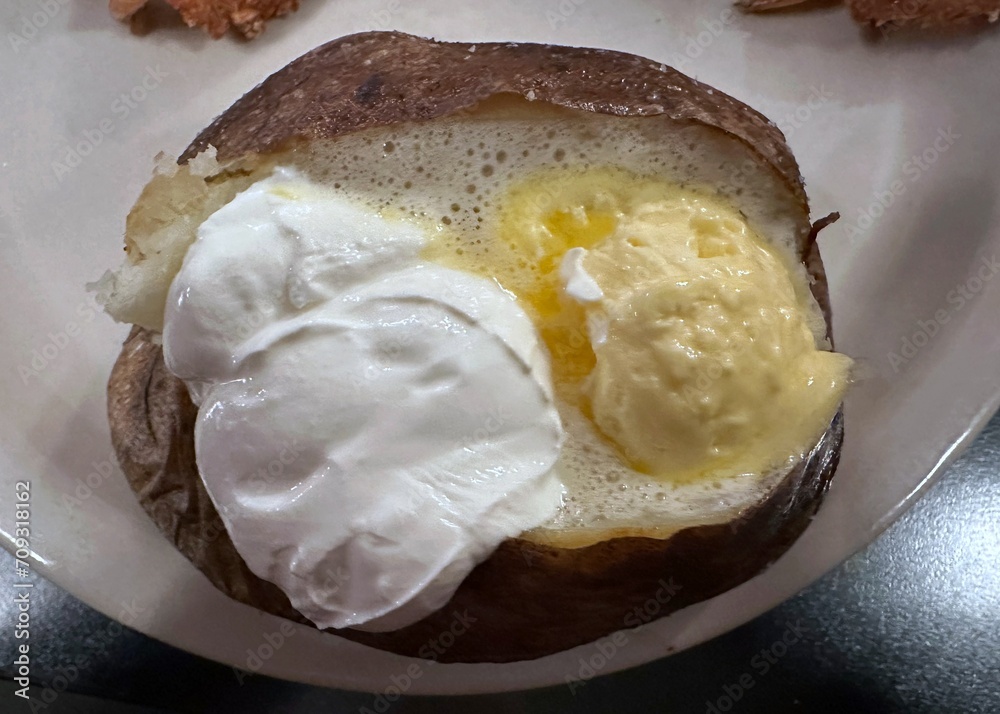 Baked russet potato with dollops of butter and sour cream Baked russet potato with dollops of butter and sour cream