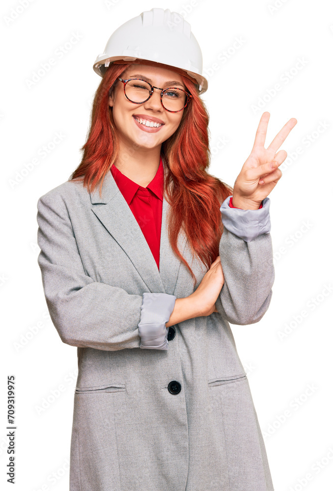 Young redhead woman wearing architect hardhat smiling with happy face winking at the camera doing victory sign. number two. Young redhead woman wearing architect hardhat smiling with happy face winking at the camera doing victory sign. number two.