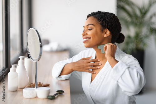 Beautiful young black woman doing neck massage with gua sha tool photo