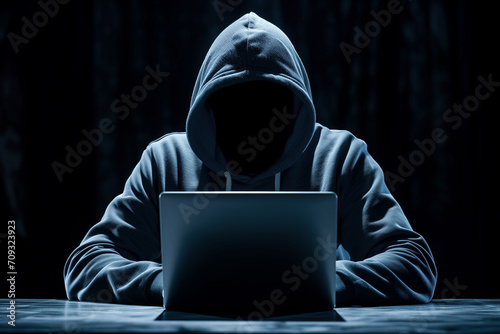 Faceless hacker in a hoodie typing on a laptop. Cyber security hacking concept.