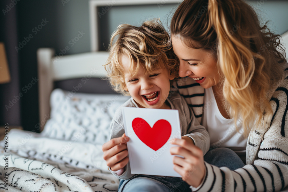 A cheerful woman and a delighted toddler engaging with a card that has a heart emblem on it, sharing a moment of happiness. A cheerful woman and a delighted toddler engaging with a card that has a heart emblem on it, sharing a moment of happiness.