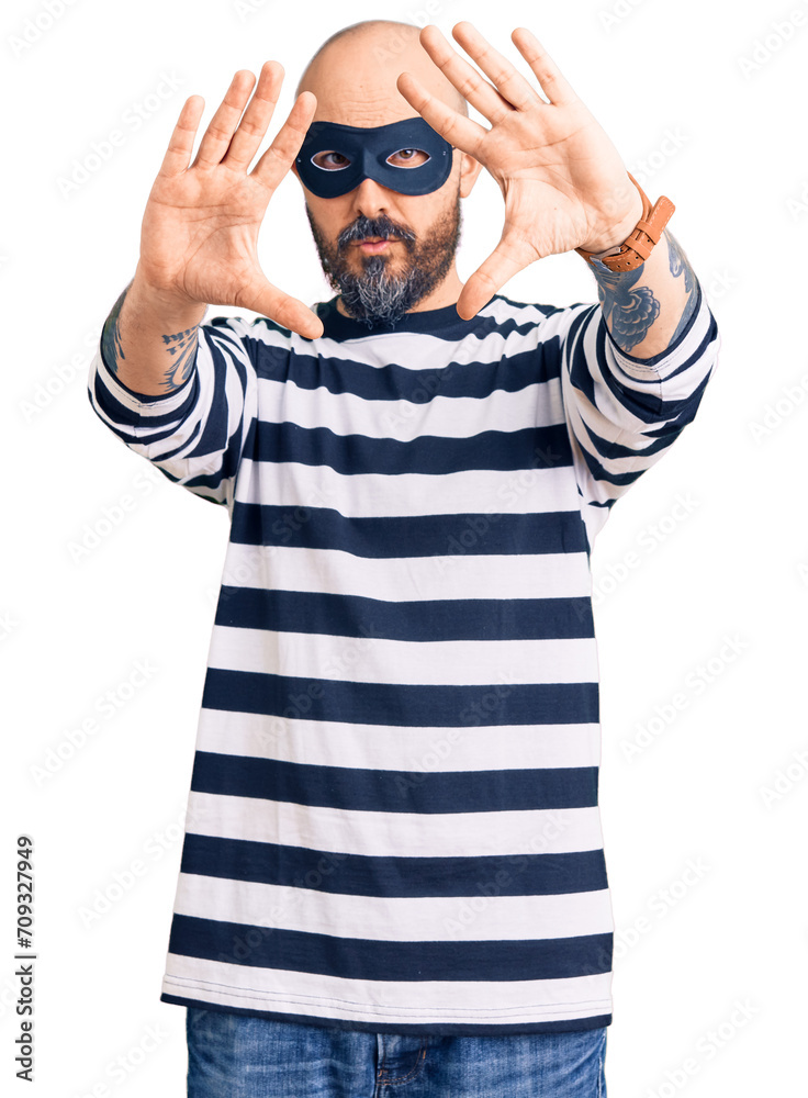 Young handsome man wearing burglar mask doing frame using hands palms and fingers, camera perspective