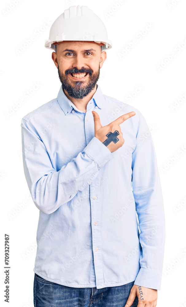 Young handsome man wearing architect hardhat cheerful with a smile of face pointing with hand and finger up to the side with happy and natural expression on face Young handsome man wearing architect hardhat cheerful with a smile of face pointing with hand and finger up to the side with happy and natural expression on face