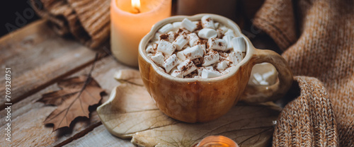 Spicy sweet fall hot drink: delicious pumpkin latte with cinnamon, marshmallow with salted caramel. Served in handmade artisan mug in shape of pumpkins, cozy home decor with candles, dry autumn leaves © ArtSys