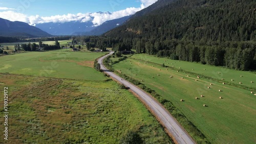 Farm road in mountain valley with motorcycle driving through, beautiful mountains and scenery with hay bails.  photo