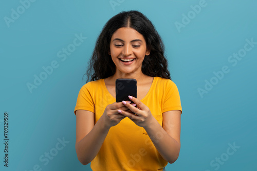 Positive young indian woman using cell phone on blue