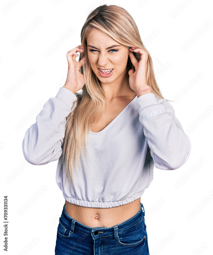 Beautiful young blonde woman wearing casual white sweater covering ears with fingers with annoyed expression for the noise of loud music. deaf concept. Beautiful young blonde woman wearing casual white sweater covering ears with fingers with annoyed expression for the noise of loud music. deaf concept.