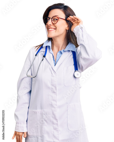 Young beautiful woman wearing doctor stethoscope and glasses smiling with hand over ear listening an hearing to rumor or gossip. deafness concept.