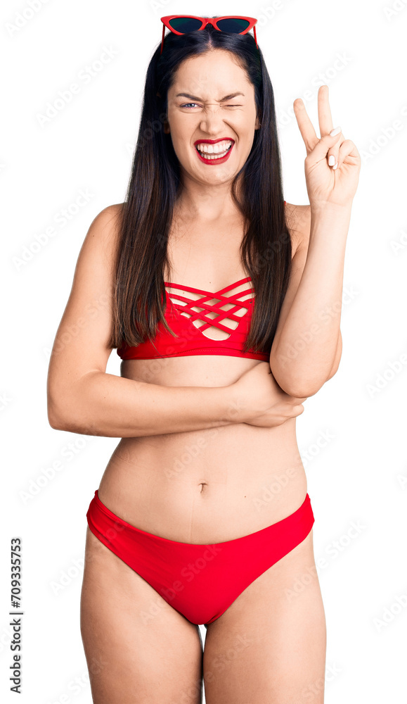 Young beautiful caucasian woman wearing bikini smiling with happy face winking at the camera doing victory sign. number two. Young beautiful caucasian woman wearing bikini smiling with happy face winking at the camera doing victory sign. number two.