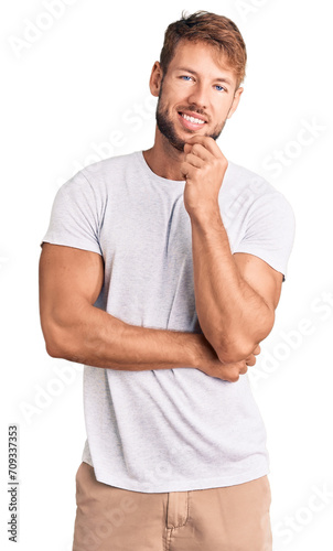 Young caucasian man wearing casual white tshirt looking confident at the camera with smile with crossed arms and hand raised on chin. thinking positive. © Krakenimages.com