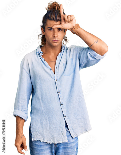 Young hispanic man wearing summer style making fun of people with fingers on forehead doing loser gesture mocking and insulting.