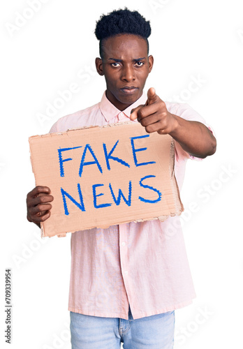 Young african american man holding fake news banner pointing with finger to the camera and to you, confident gesture looking serious © Krakenimages.com