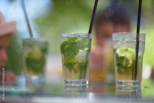Refreshing green lemonade in a glass on the table against the background of nature. Freshly squeezed drinks with ice. Lemonade with lemon, mint lime and herbs
