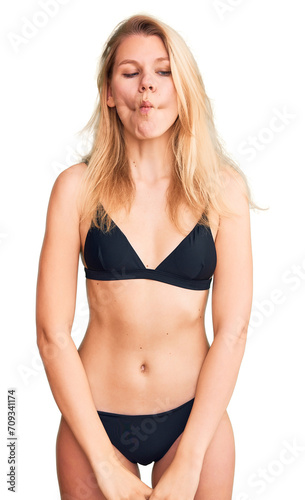 Young beautiful blonde woman wearing bikini making fish face with lips, crazy and comical gesture. funny expression.