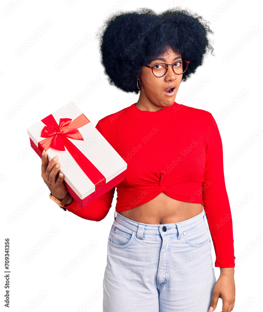 Young african american girl holding gift in shock face, looking skeptical and sarcastic, surprised with open mouth Young african american girl holding gift in shock face, looking skeptical and sarcastic, surprised with open mouth
