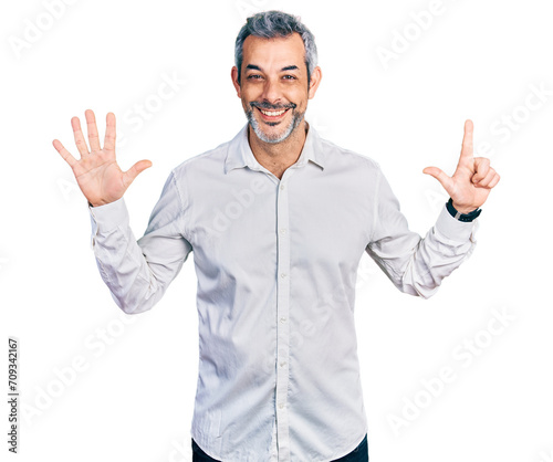 Middle age hispanic with grey hair wearing casual white shirt showing and pointing up with fingers number seven while smiling confident and happy.