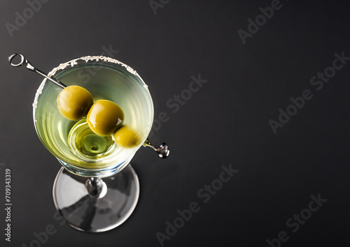 closeup photo of fresh cold martini cocktail glass with gin and olive isolated on black background. top angle