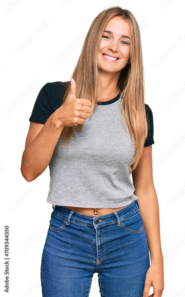 Young blonde woman wearing casual clothes doing happy thumbs up gesture with hand. approving expression looking at the camera showing success. Young blonde woman wearing casual clothes doing happy thumbs up gesture with hand. approving expression looking at the camera showing success.
