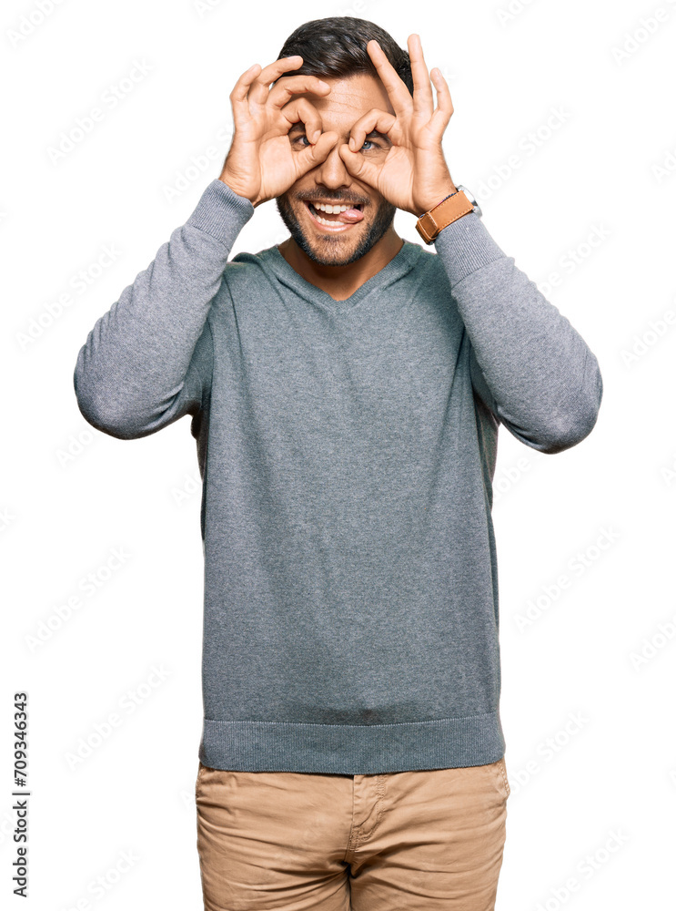 Naklejka premium Handsome hispanic man wearing casual clothes doing ok gesture like binoculars sticking tongue out, eyes looking through fingers. crazy expression.