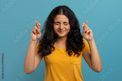 Excited young indian lady with closed eyes and crossed fingers photo