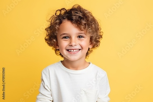 Portrait of a cute curly little boy smiling at camera over yellow background