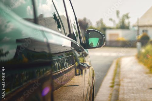 rückspiegel eines pkw auf einem parkplatz neben einem haus bei strahlender sonne mit stahlen