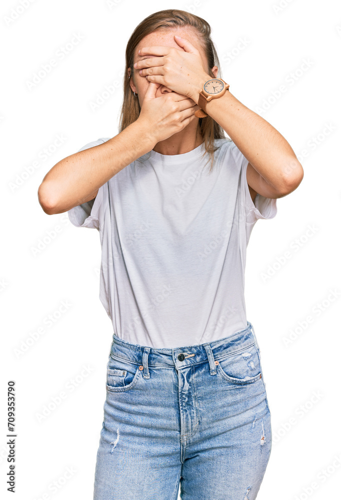 Beautiful young blonde woman wearing casual white t shirt covering eyes and mouth with hands, surprised and shocked. hiding emotion Beautiful young blonde woman wearing casual white t shirt covering eyes and mouth with hands, surprised and shocked. hiding emotion