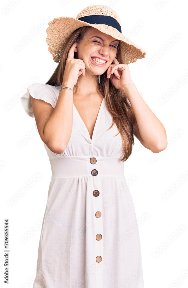 Young beautiful blonde woman wearing summer dress and hat covering ears with fingers with annoyed expression for the noise of loud music. deaf concept. Young beautiful blonde woman wearing summer dress and hat covering ears with fingers with annoyed expression for the noise of loud music. deaf concept.