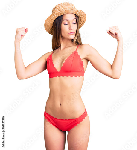 Beautiful brunette young woman wearing bikini showing arms muscles smiling proud. fitness concept.