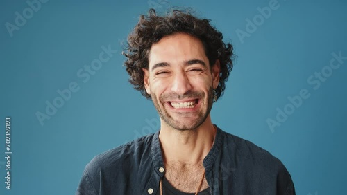 Close up, laughing man looks at camera isolated on blue background in studio photo
