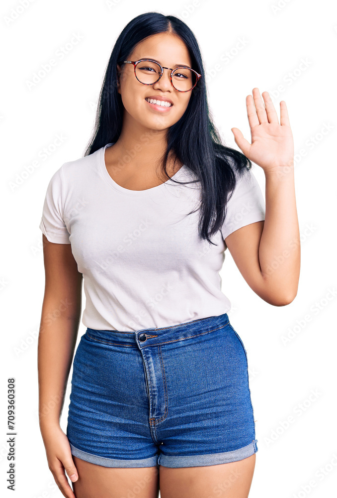 Young beautiful asian girl wearing casual clothes and glasses waiving saying hello happy and smiling, friendly welcome gesture Young beautiful asian girl wearing casual clothes and glasses waiving saying hello happy and smiling, friendly welcome gesture