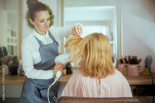 pensive woman hair salon worker blowout hair with hair dryer