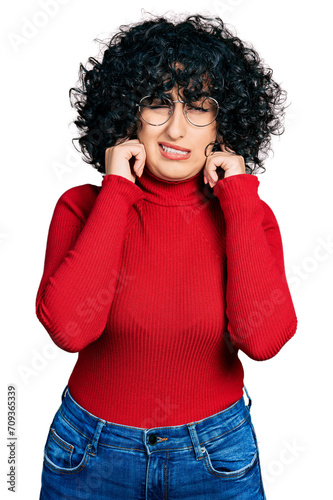 Young middle east girl wearing casual clothes and glasses covering ears with fingers with annoyed expression for the noise of loud music. deaf concept.