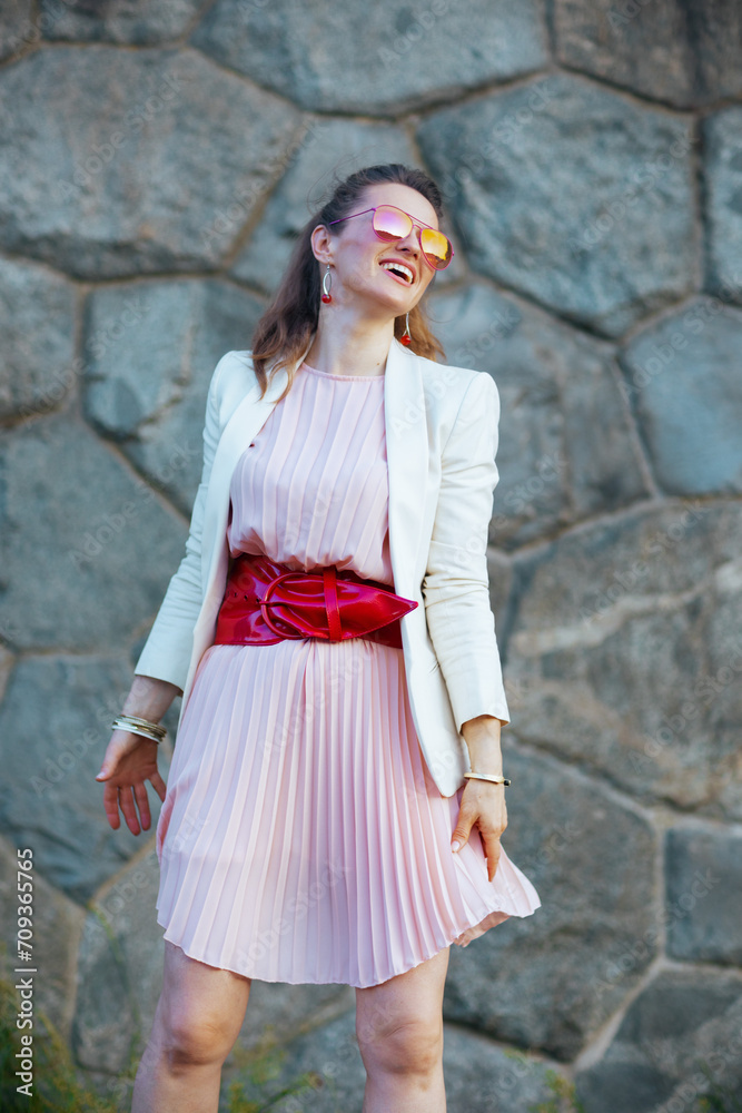 happy stylish woman in pink dress and white jacket in city