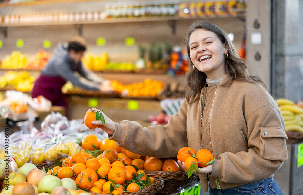Happy young girl chooses and buys ripe delicious tangerines in grocery section of the supermarket
