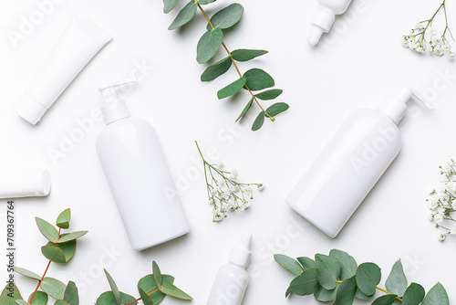 Set of organic eco skin care products in white unbranded containers , beautiful flowers and eucalyptus leaves on white background top view. Cosmetic branding concept. photo