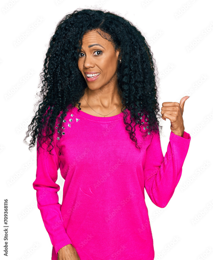 Middle age african american woman wearing casual clothes smiling with happy face looking and pointing to the side with thumb up. Middle age african american woman wearing casual clothes smiling with happy face looking and pointing to the side with thumb up.